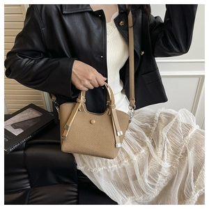 Khaki woven bucket bag with leather handle shown with elegant dress and leather jacket