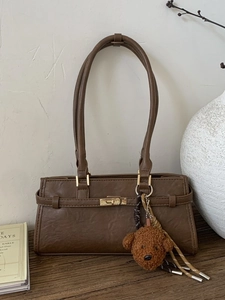 Retro coffee brown shoulder bag with metal lock, plush dog pendant on wooden table
