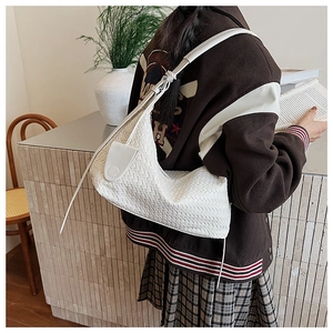 White woven shoulder bag shown in a lifestyle setting, detailing the texture and charm