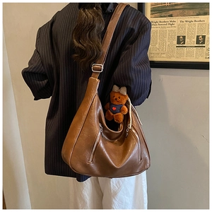 Close-up of a brown leather Hobo bag with zipper details and a cute bear charm