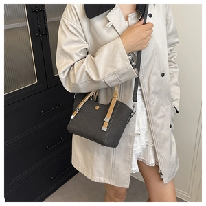 Detail of black woven texture bag with khaki leather handles on a beige coat model