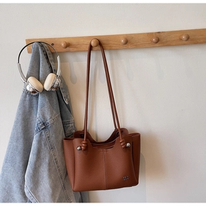 Vista dettagliata della borsa a secchiello in pelle marrone con trama litchi e nodi decorativi