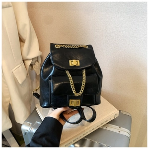 Detailansicht eines schwarzen PU-Rucksacks mit Goldkette und Drehverschluss auf Koffer