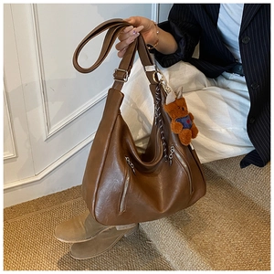 Detailed view of brown leather tote bag with functional zippers and cute plush bear charm