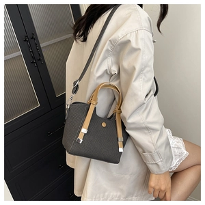 Close-up of a grey woven bucket bag with brown handles held by a model in a trench coat