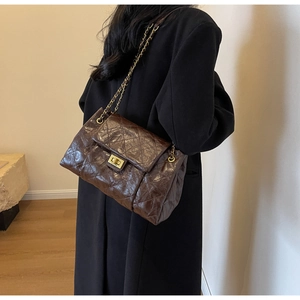 Detail of dark brown quilted crossbody bag with gold chain strap and metal turn-lock closure