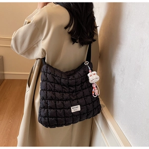 Close-up of black quilted puffer tote bag with plush bunny charm and branded logo tag