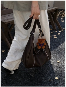 Close-up of a vintage dark brown leather tote bag with metallic zippers and bear charm