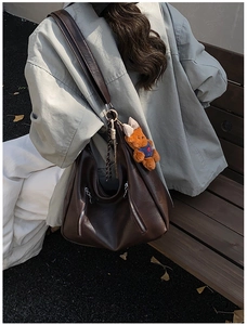 Detail of dark coffee brown hobo bag featuring decorative zippers and a cute plush bear charm