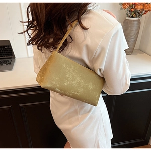 Detailed macro view of the gold textured shoulder bag featuring an embossed brand logo