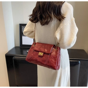 Deep red quilted chain bag shown over a white knit dress in a minimalist room setting