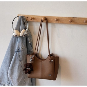 Dettaglio di una borsa tote in pelle marrone con un simpatico ciondolo a orsetto