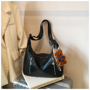 Detail of a black leather hobo bag with zip accents and a cute teddy bear charm accessory