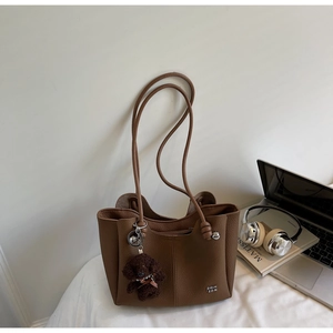 Borsa tote in pelle marrone con ciondolo a orsetto su letto bianco con accessori