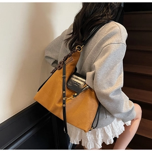 Close-up of brown suede tote bag featuring black leather straps and peace sign charm