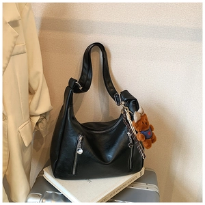 Detail of a large black leather hobo bag with front zippers and a cute teddy bear charm