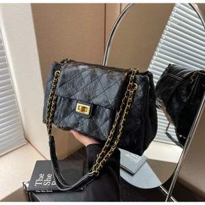 Detailed close-up of retro black quilted leather with a gold chain strap and square metal lock