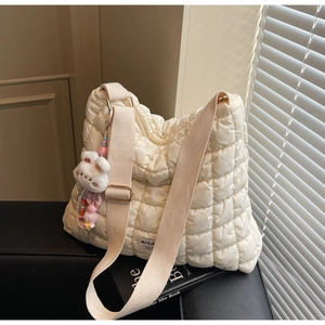 Detailed macro view of cream quilted tote bag with wide strap and rabbit charm accessory