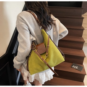 Detailed shot of an avocado green suede tote bag with brown leather trim and metal clasp