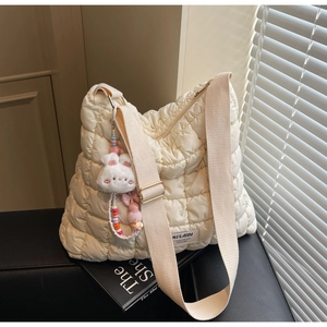 Detail of cream quilted tote bag featuring plush bunny charm and wide fabric shoulder strap
