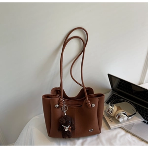 Dettaglio borsa tote in pelle marrone con ciondolo a cucciolo e logo metallico chic