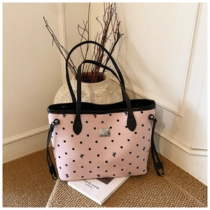 Close-up of pink polka dot canvas tote bag featuring metal logo plate and black leather handles