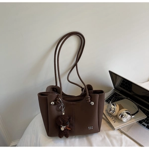 Dettaglio borsa a secchiello in pelle marrone scuro con ciondolo a orso e logo in metallo