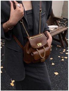 Detail eines braunen Lederrucksacks mit goldenen Kettenriemen und Drehverschlüssen