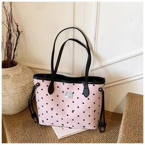 Detail of pink polka dot tote bag with silver logo plate on a rustic woven mat