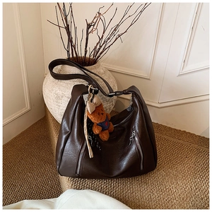 Detail of dark brown leather tote featuring vertical zippers and plush bear charm