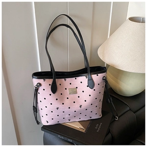 Detailed view of pink polka dot tote bag with leather handles and metallic logo plate