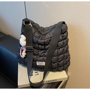 Detail of black quilted tote bag with wide canvas strap and plush rabbit charm accessory