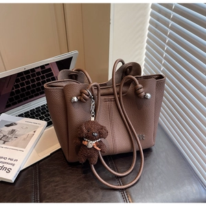 Dettaglio della borsa tote in pelle marrone scuro con ciondolo a orsetto e doppi manici