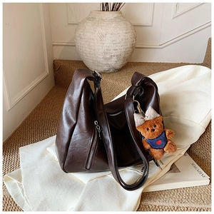 Detail of dark brown faux leather tote bag with soft pleats and a cute teddy bear charm