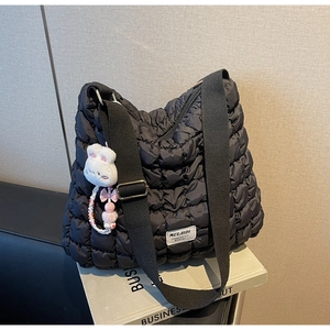Detail of black quilted puffer tote bag with adjustable strap and plush rabbit charm