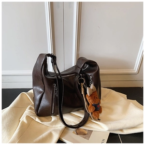 Detail of dark brown leather tote bag with vertical zippers and cute bear charm