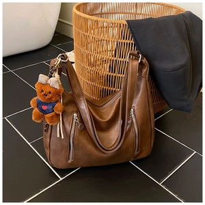 Close-up of brown leather hobo bag with silver zippers and a cute plush bear charm