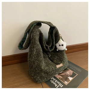 Detail of dark green fuzzy tote bag with plaid lining and a white eye-shaped pompom charm