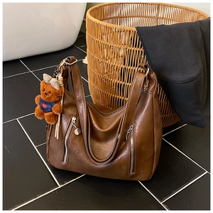 Detail of dark brown vintage faux leather tote bag with silver zippers and bear charm