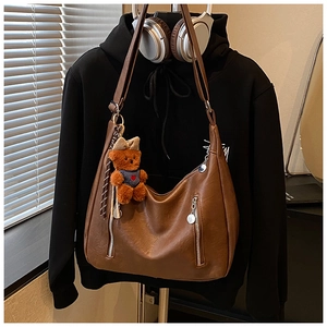 Detailed view of a brown hobo bag with pebble leather texture and a cute plush bear charm