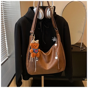 Close-up of vintage brown leather bag with metallic zippers and a cute plush bear charm