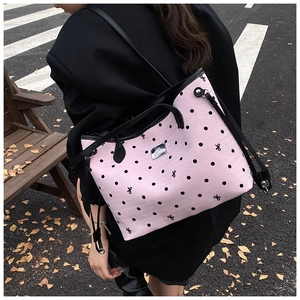 Detail of pink polka dot tote bag showing black shoulder straps and metal logo plate