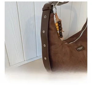 Detail of suede shoulder bag with adjustable eyelet strap and wooden bead charm