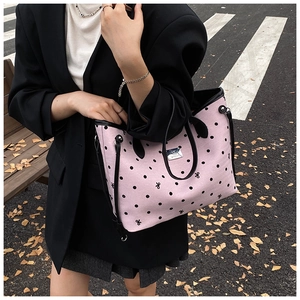 Detail of pink polka dot tote bag with black faux leather handles and metal logo plaque