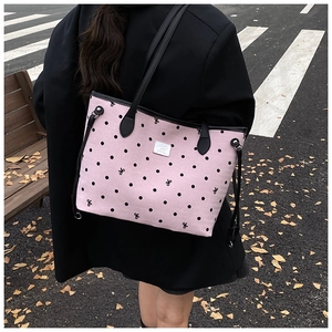 Pink polka dot tote bag with black handles shown in an autumn street setting