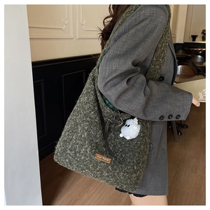 Detail of dark green tweed tote bag with a white fur ball charm and leather logo patch