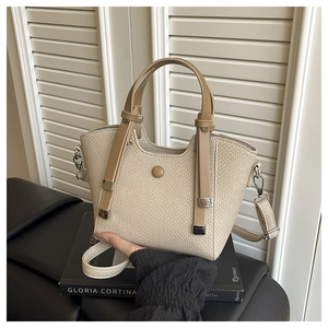 Detail view of woven cream bucket bag with brown leather handles and magnetic closure