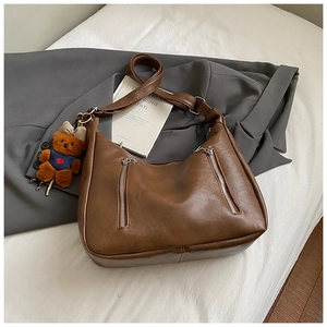 Close-up of brown vintage leather bag with silver zippers and a cute teddy bear charm
