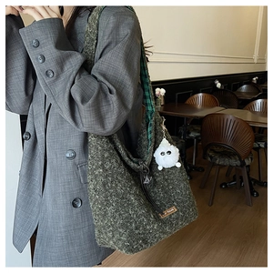 Close-up of deep green woolen tote bag featuring check lining and a white plush charm