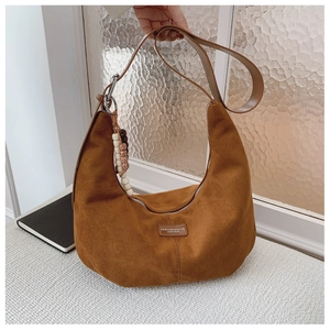 Detail of brown faux suede hobo bag featuring a wooden bead charm and leather brand tag
